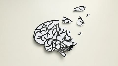 A paper brain sketch with black lines is torn, scattering fragments upward on a beige background.