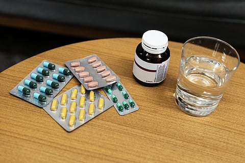 Few strips of different tablets and a glass of water on a bedside table.