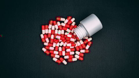 Top view shot of red-and-white capsules falling from the small pill bottle on the dark background. 