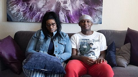 A woman and a young man sit on a sofa with neutral expressions. 