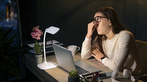 Medium shot woman working late at night, sitting at a desk.