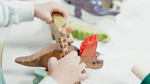 A child's hands play with colorful wooden animal toys on a light table.