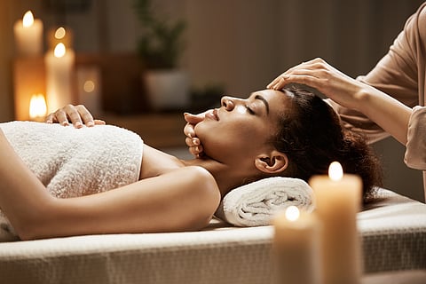 A woman getting a massage on her face and neck with some lit candles in the background. 