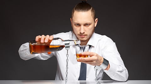 A man with a stern expression pours whiskey into a glass, both handcuffed with chains.