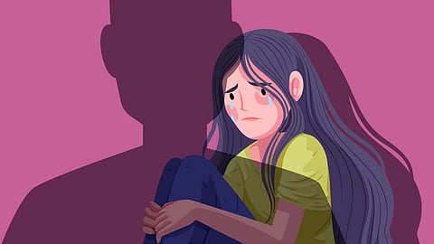 A sad girl with long hair sits hugging her knees, a large shadow looms over her.