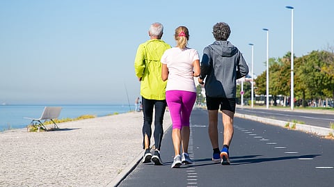 Three people jog along a scenic waterfront path on a clear day.