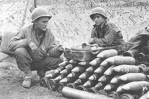 Black and white photo showing two soldiers sitting near a collection of shells. 