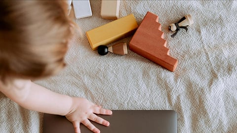 Close-up of a toddler’s hand resting on a metal surface, surrounded by colorful wooden blocks and small toys.