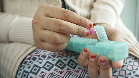 A woman filling a pill organizer with a pink tablet.