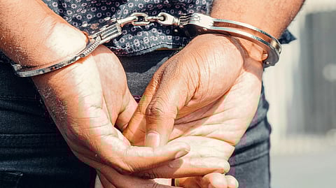 Close-up of a person’s hands being handcuffed, wearing blue jeans and a blue printed shirt.