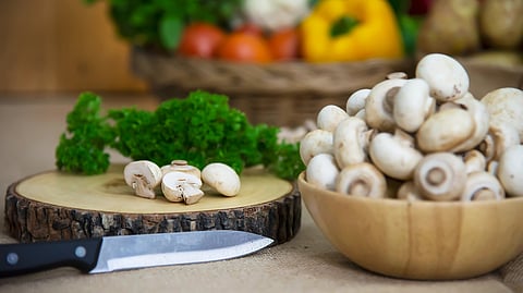 A wooden bowl of fresh mushrooms sits beside a chopping block.