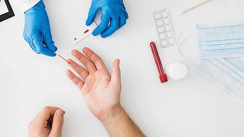 A medical professional in blue gloves uses a rapid test device on a patient's finger.