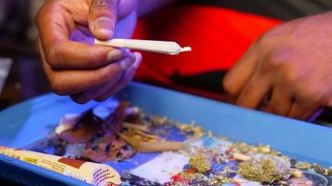 A hand holds a freshly rolled joint and more drugs.