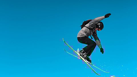 Ski jumping athlete, wearing grey ski suit and making high jump. 