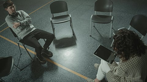 A client sitting on left and a therapist sitting on the right, surrounded by chairs.