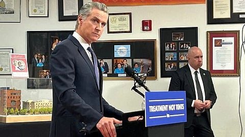 A man in a suit stands at a podium labeled “Treatment Not Tents."