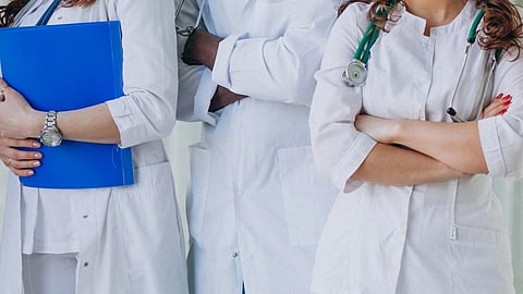 A group of five smiling healthcare professionals, wearing white coats and stethoscopes.