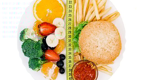 Plate split by a measuring tape showing healthy fruits and vegetables on one side and a burger with fries on the other.