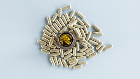 An open amber bottle with yellow capsules inside is surrounded by beige capsules.
