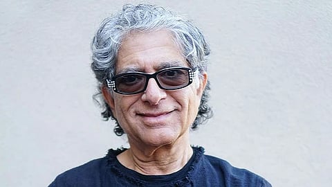 Portrait of Deepak Chopra smiling while wearing goggles and a blue t-shirt he has grey hairs.