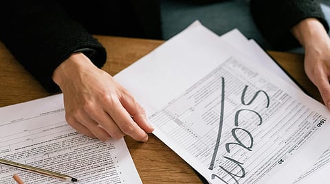 Close-up of a person’s hands holding a stack of official-looking documents, with the word “SCAM” clearly written on one page.