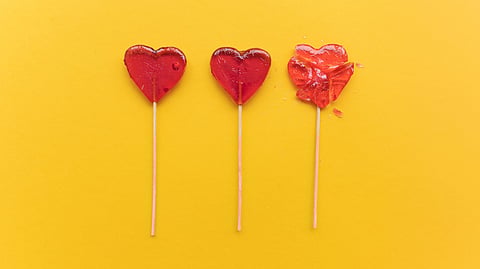 Three red heart-shaped lollipops on a bright yellow background. 
