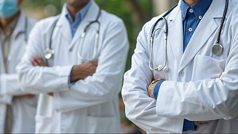 Three doctors standing in a row with white coats and stethoscopes around their neck.