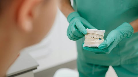Close-up of a dentist holding a teeth model wearing green scrubs.