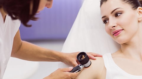 A dermatologist examines a woman's shoulder using a dermatoscope.