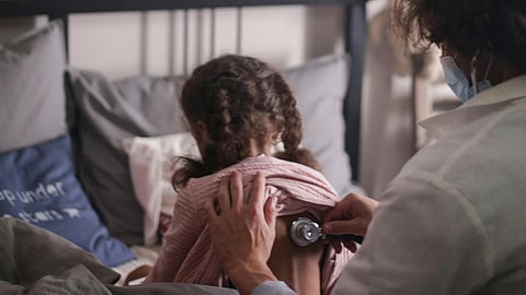 Close-up of a stethoscope placed over a girl's back by a physician.