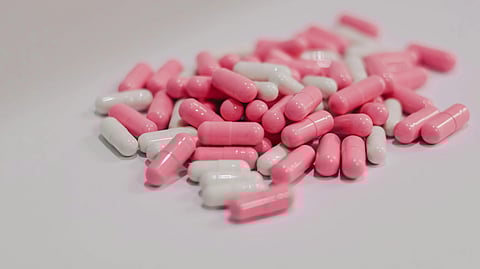 Close-up of a pile of pink and white capsules over a white background.