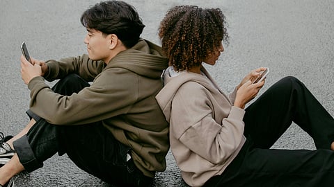 A boy and a girl sitting with their back to each other and using their phones.