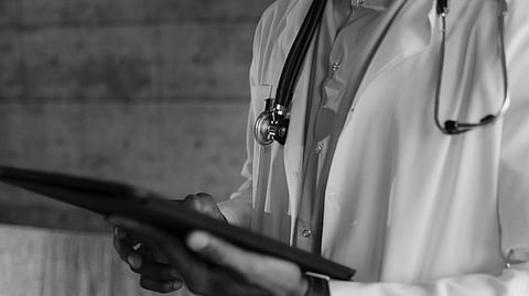 A doctor wearing white coat , stethoscope around neck and holding a tab.