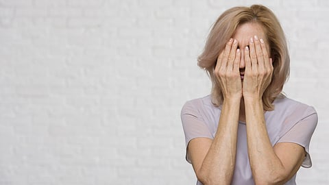 A middle-aged lady covering her face with her hands.