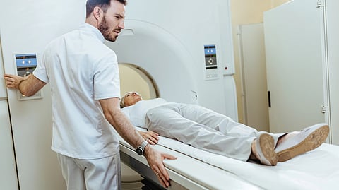 A man lying down on the MRI machine to get a scan and another one is operating the machine. 