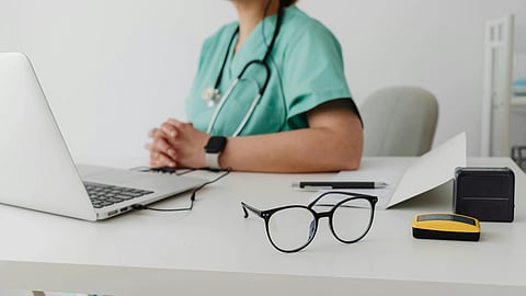 A doctor sitting in front of a laptop and specs kept on table.
