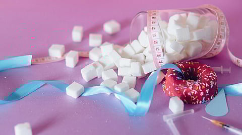 Sugar cubes and donut kept with a measuring tape on pink background.