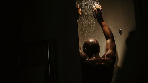 Person standing in a dim shower with water flowing.