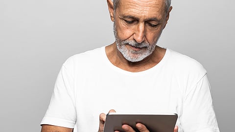 An older man in a white T-shirt intently looks at a tablet.
