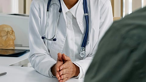 A focused doctor with a stethoscope speaks to a patient in an office. 