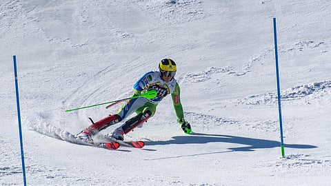 A skier in blue and green races down a snowy slope.