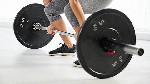 A person wearing gray leggings and black sneakers performs a deadlift.