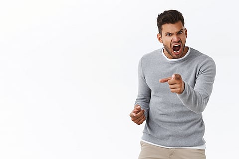 An angry young man wearing a grey sweater. 