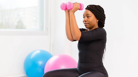 A woman in a black workout outfit lifts pink dumbbells.