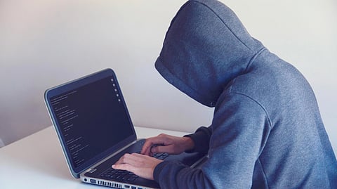 A person wearing a hoodie and working on laptop.