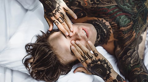 Man with colorful tattoos resting on a white sheet