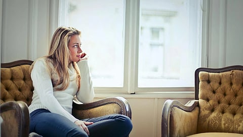 A woman thinking and sitting on a sofa and looking out of the window.