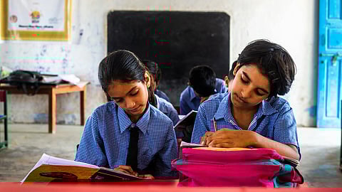 2 students, one girl and one boy, sitting next to each other in blue school uniform.
