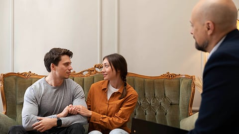 A couple sits on a couch, sharing supportive glances during a therapy session.