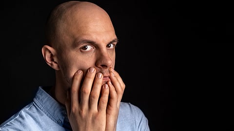 A bald man with a concerned expression holds his hands over his mouth.